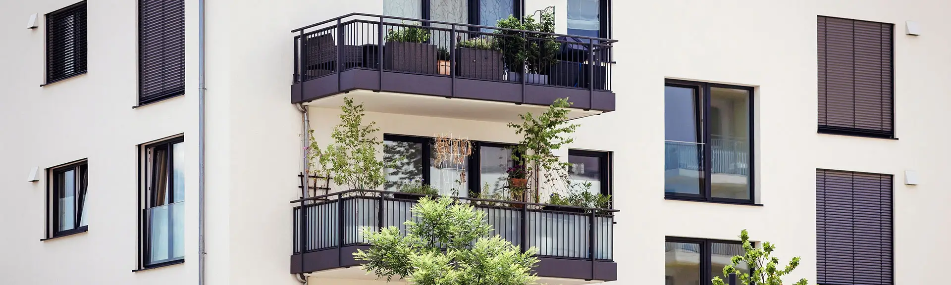 Mehrfamilienhausfassade mit Balkonen und geschlossenen Raffstores an den Fenstern