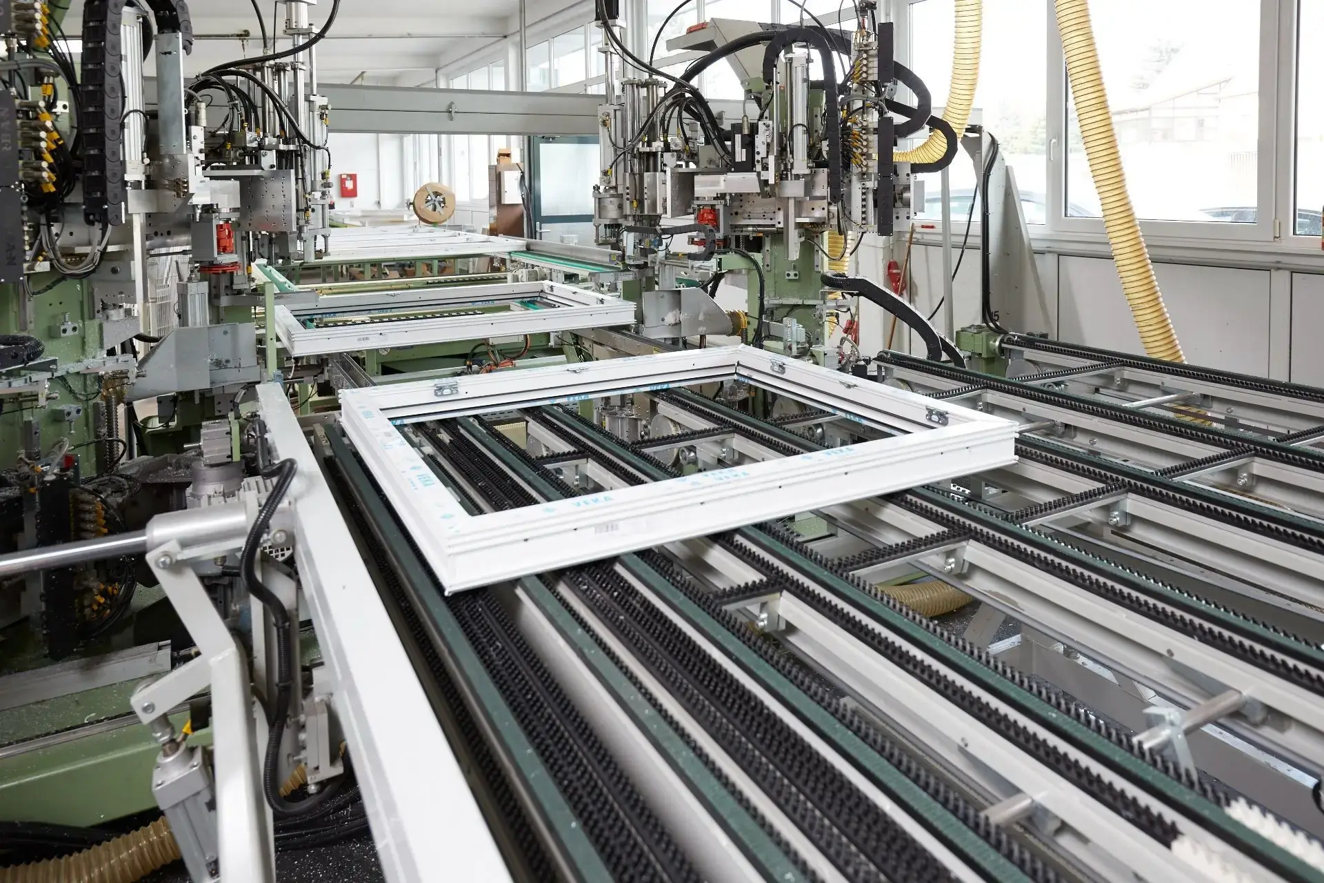 Weiß & Sohn Glaserei und Fensterbau: Fensterproduktion Fertigungslinie mit mehreren weißen Fensterrahmen und automatisierten Maschinen in einer hellen Werkhalle