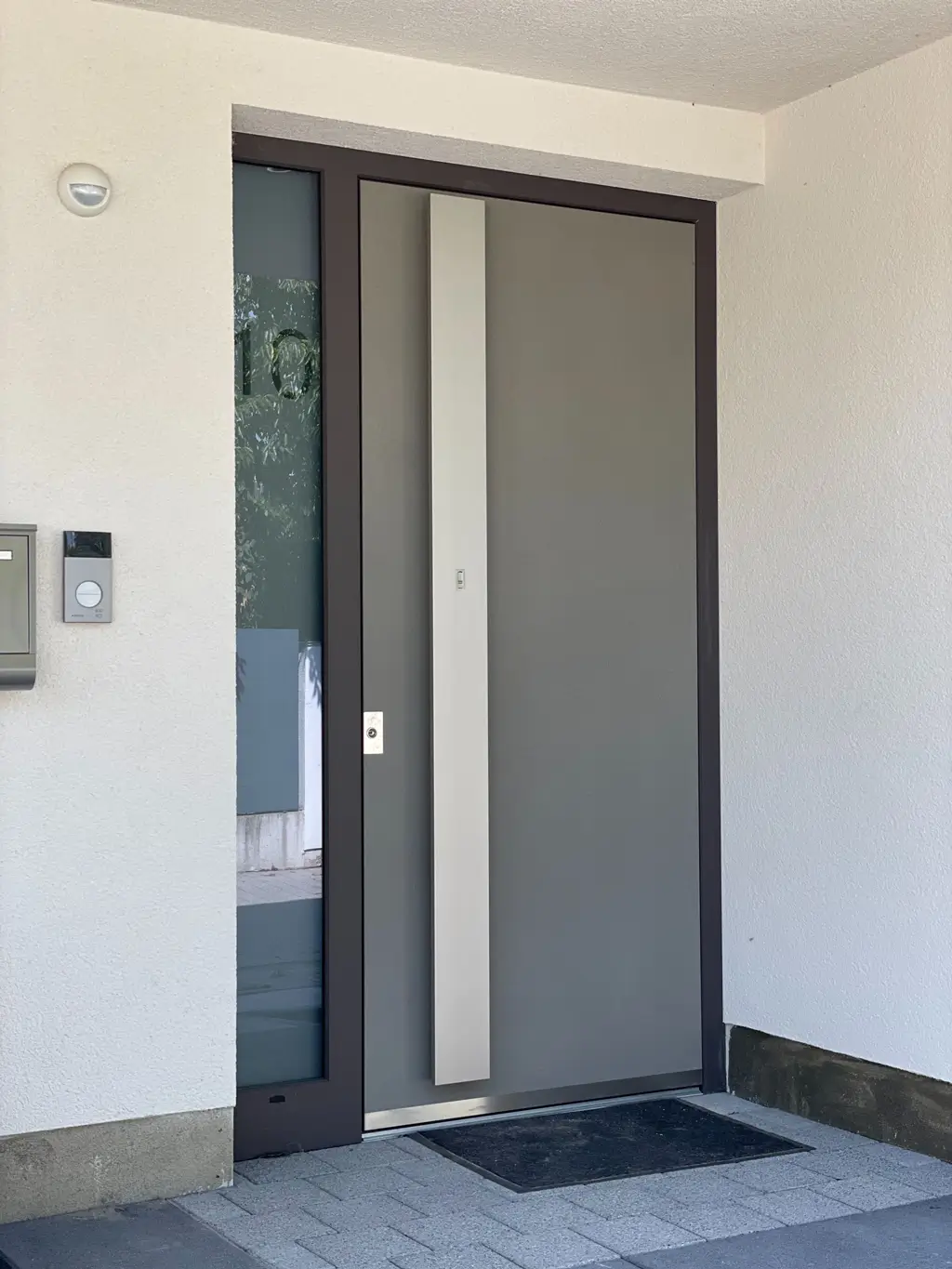 Weiß & Sohn Glaserei und Fensterbau: moderne Haustür Moderner Hauseingang mit grauer Tür, schmalem Seitenfenster und Briefkasten an der weißen Wand