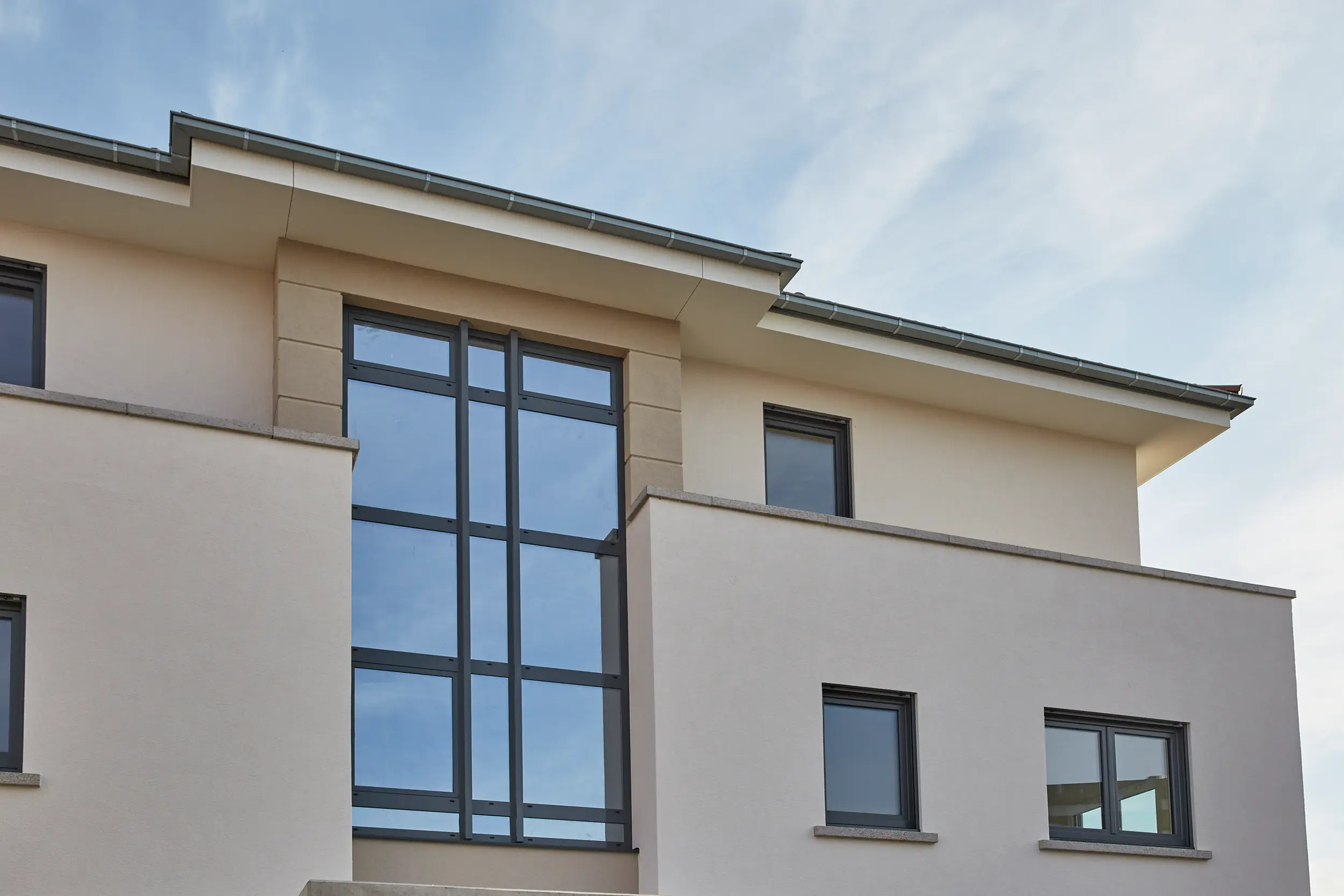 Fassade eines modernen Wohnhauses mit großen Fenstern und Flachdach unter bewölktem Himmel