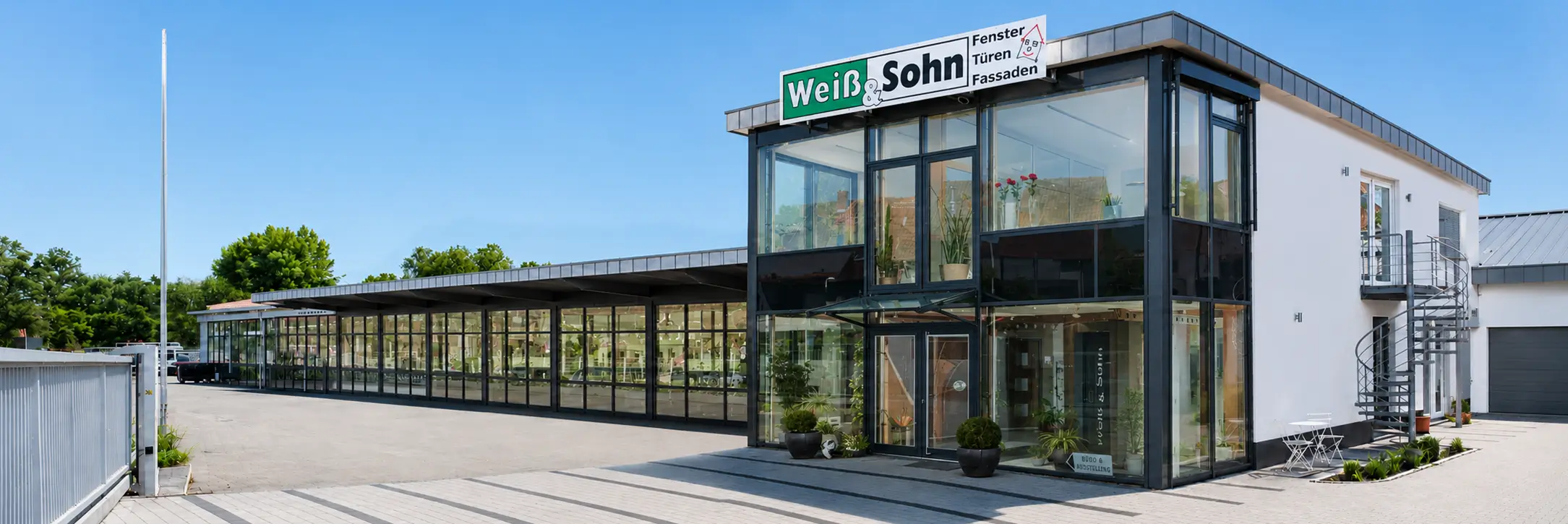 Modernes Bürogebäude mit Glasfassade und Flachdach, auf dem ein Schild mit der Aufschrift 'Weiß & Sohn' steht