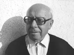Porträt eines älteren Mannes mit Brille, Hemd und Pullover vor einer hellen Wand