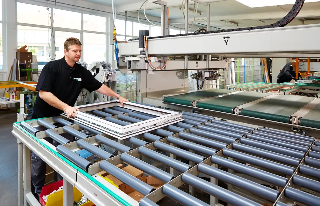 Mann in schwarzem Poloshirt bedient Maschine mit Förderband und Metallrahmen in Produktionshalle